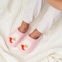 Wearing The Darling Effect’s Santa Fuzzy Slippers, a person in white pants relaxes with their feet up on a textured white blanket.