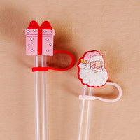 The Darling Effect's Jolly Santa Straw Topper Set includes two clear straws with festive silicone toppers—a pink present with a red bow and a smiling Santa—perfect for adding cheer to your leak-resistant drinkware.