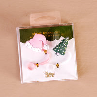 The Darling Effect’s Santa Baby Straw Topper Set includes two leak-resistant silicone toppers—a pink Santa hat and a green Christmas tree—perfect for adding festive charm to your drinkware. Packaging says “straw topper set” and “the darling effect.”.
