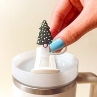 A hand with light blue nails holds The Darling Effect's Santa Baby Straw Topper Set on a straw above a white insulated cup, showing how these festive accessories add charm to your leak-resistant drinkware.