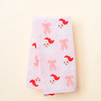 Light pink Dear Santa Tea Towel featuring a repeating pattern of Santa Claus faces and bows.