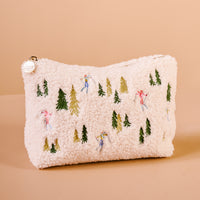 The Darling Effect Aprés Ski Teddy Pouch is an off-white sherpa fabric zippered pouch embroidered with colorful skiers and evergreen trees.