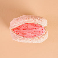 The Darling Effect's Square Holiday Gift Bow Red Teddy Pouch is a small, fluffy pouch with a pink interior featuring "merry" in red script—perfect as a festive organizer for the holidays.