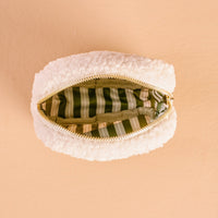 The Square Twinkling Tree Teddy Pouch by The Darling Effect, a small white sherpa pouch, is open to reveal its green interior lining with white and tan vertical stripes, set against a peach-colored background.