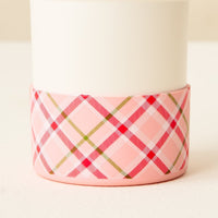 The Darling Effect’s Festive Plaid Tumbler Silicone Boot, with a pink background and red, green, and white plaid pattern, is perfect for adding charm to your tumbler accessories or personalizing your silicone boot designs.