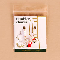 The Home for the Holidays Tumbler Charm by The Darling Effect features gold, pearl, gingerbread man, red cup, and festive tumbler charms on a card—perfect for gifting this season. Displayed on a light tan background.