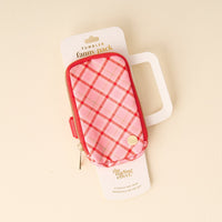 A small pink and red plaid Festive Plaid Tumbler Fanny Pack by The Darling Effect is attached to white packaging with a handle cutout and gold text, displayed on a light beige surface.