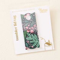 A packaged Jolly Sprig Green Tumbler Lid Tag from The Darling Effect, featuring a dark background with pink florals and green leaves. The packaging displays "Tumbler Lid Tag" and "The Darling Effect" in gold on a white background.