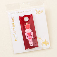 The Nutcracker Tumbler Lid Tag by The Darling Effect features a pink nutcracker on a red background with gold "tumbler lid tags" and "the darling effect" lettering. Fits Stanley Quencher 2.0—perfect for holiday tumbler accessories.