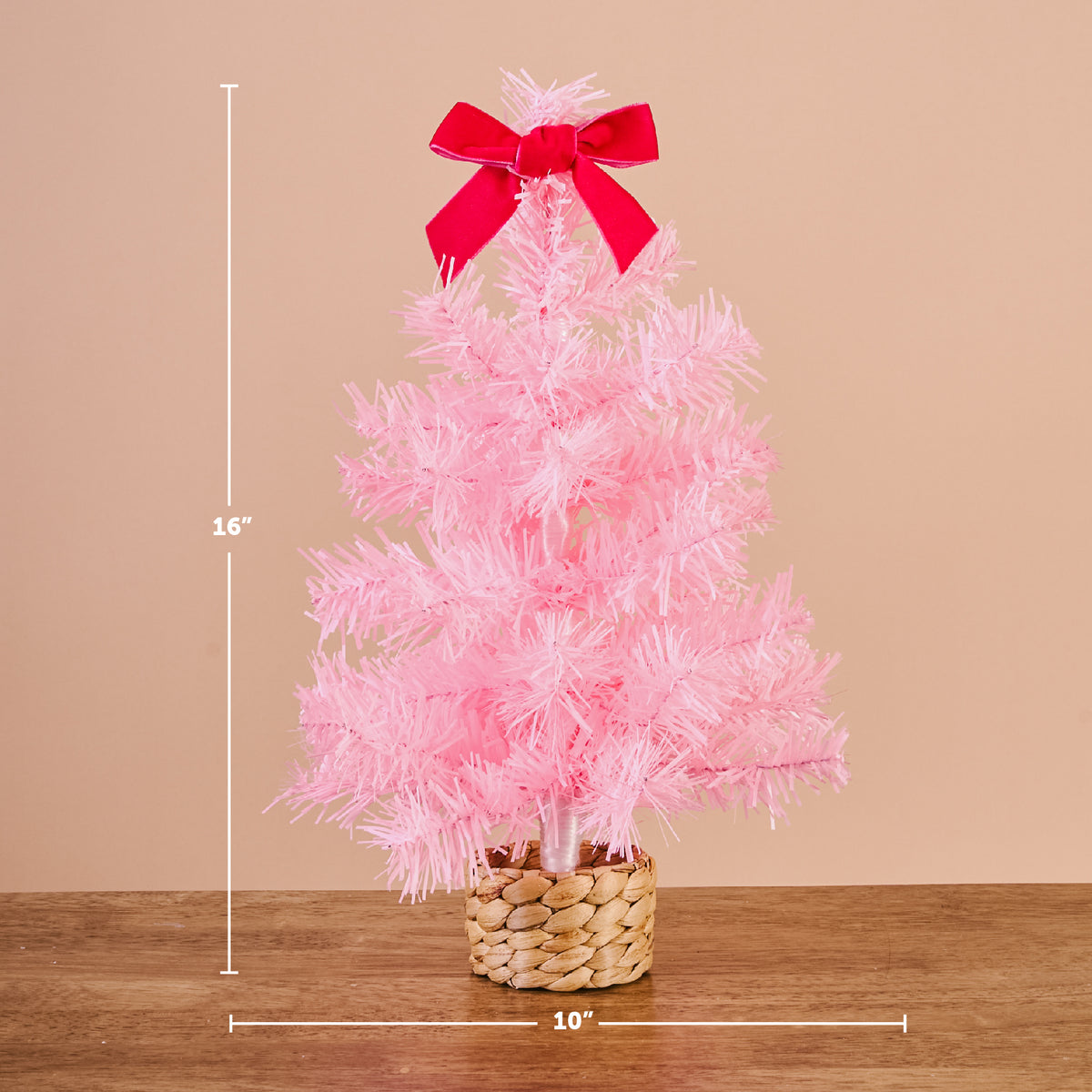 A 16-inch tall Pink Mini Artificial Christmas Tree with a red bow on top, set in a 10-inch wide woven basket base for festive holiday décor.