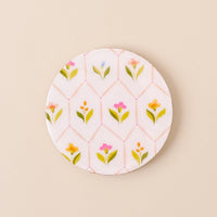 A round ceramic plate with a white background and pastel floral pattern is paired beautifully with the-darling-effect's Handpicked for You Wood Enamel Coaster on a beige surface.