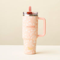 The-darling-effect’s Mama Peach 40 oz Lifestyle Flip Straw Tumbler, a tall light pink cup with small white flowers, “mama” text, and a right-side handle, sits on a white surface against a beige background.