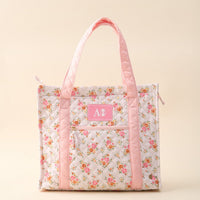 The Darling Effect's Alpha Phi The Everyday Quilted Tote Bag features a floral quilted design, light pink handles and trim, a front pocket with white Greek letters on a pink patch—ideal for displaying your sorority pride in style.