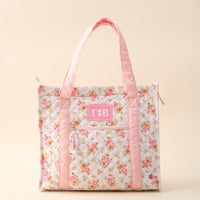 The Darling Effect Gamma Phi Beta The Everyday Quilted Tote Bag is a stylish, spacious quilted tote with pink handles, floral pattern, front zip pocket, and a pink patch embroidered with white Greek letters.