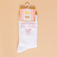 Gamma Phi Beta Embroidered Crew Socks by The Darling Effect feature pink cursive lettering and a small pink bow, hanging on a white hanger with a pink and gold tag—perfect for showing your sorority spirit.