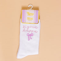 Sigma Kappa Embroidered Crew Socks by The Darling Effect: white socks feature pink Sigma Kappa embroidery, a bow, and come with a lavender and gold tag labeled "that's so sorority spirit SOCKS.