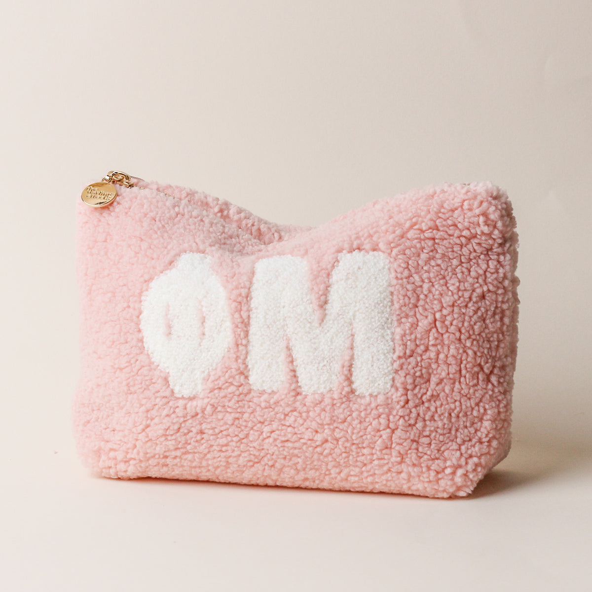 The Darling Effect’s Phi Mu Blush Teddy Letter Pouch, a pink sherpa zip pouch featuring white Phi Mu Greek letters on the front, is perfect as a sorority accessory or makeup organizer and is pictured against a plain light background.