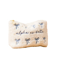 A white, fluffy zippered pouch decorated with blue embroidered bows, small pearls, and the words alpha xi delta stitched on the front.