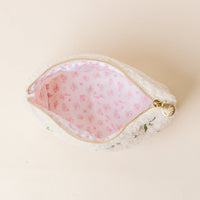 The Kappa Delta Bows & Pearls Teddy Pouch by The Darling Effect is a small white sherpa pouch with a gold zipper and pink floral lining—perfect as a cozy sorority gift. It's shown open on a light beige surface.