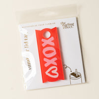 The Darling Effect XOXO Tumbler Lid Tag features a red design with XOXO and a pink heart, made for Stanley Quencher 2.0 lids. Packaged on an “ACCESSORIZE YOUR TUMBLER” card—cute, personalized accessories to brighten your day!.