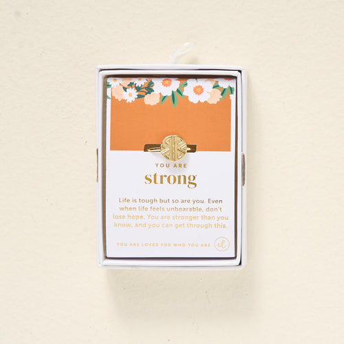 The Darling Effect’s You Are Strong Adjustable Ring comes in a white box with an orange floral background. The card says: YOU ARE strong. Life is tough, but so are you—you’re stronger than you know and will get through this.