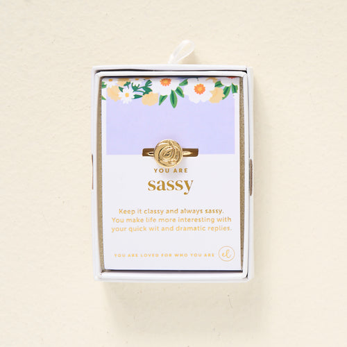The Darling Effect’s You Are Sassy Adjustable Ring features a 14k gold leaf design on a card reading “You Are Sassy” and gold foil text: “Keep it classy and always sassy. You make life interesting with your quick wit.”.