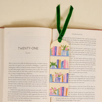An open book displaying chapter twenty-one with the Book Shelfie Acrylic Bookmark on top, featuring bookshelf and plant illustrations plus a green velvet ribbon—an ideal gift for book lovers.
