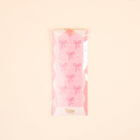The-darling-effect’s Bows Pink Acrylic Bookmark features pink bows and white dots, packaged in clear plastic with a cream background—a delightful gift for book lovers and collectors of cute bookmarks.