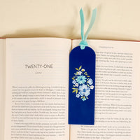 An open book displays a chapter titled TWENTY-ONE with the-darling-effect’s Dainty Floral Navy Acrylic Bookmark, featuring painted blue and white flowers and a velvet ribbon tassel—an enchanting gift for book lovers resting on the right page.