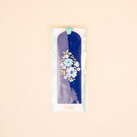 The "Dainty Floral Navy Acrylic Bookmark" by the-darling-effect features a white and blue floral design, turquoise velvet ribbon tassel, and comes in a clear plastic sleeve—a perfect gift for book lovers, shown on a light beige background.