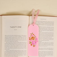 An open book lies flat with the Dainty Floral Pink Acrylic Bookmark—featuring floral designs and two pink ribbons—resting on its pages, making a charming gift for book lovers. The visible chapter is titled TWENTY-ONE.