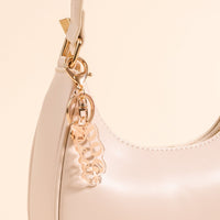 Close-up of The Darling Effect’s shiny light beige handbag with gold hardware, featuring a Dog Mom Acrylic Keychain accessory on the strap, set against a soft beige background.