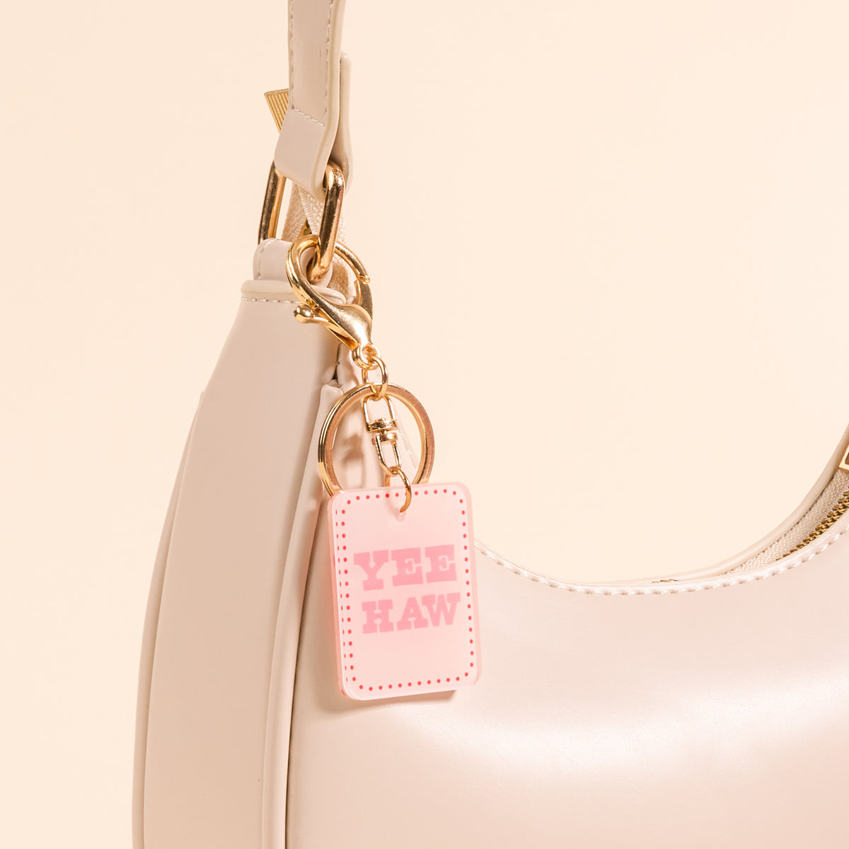 A close-up of the-darling-effect’s Yeehaw Acrylic Keychain in pink, attached to a light beige handbag—perfect for anyone who loves cute accessories.