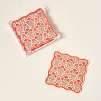 The Darling Effect's Everbloom Dusty Rose Table Talk Acrylic Coaster Set features two floral coasters in red, pink, and green with scalloped edges—one displayed in a clear acrylic holder, ideal for stylish table decor.