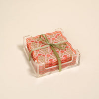 The Darling Effect’s Everbloom Dusty Rose Table Talk Acrylic Coaster Set features pink floral coasters with orange blooms, tied with a green ribbon in a clear acrylic holder—perfect for adding fresh style to your table.