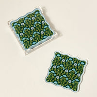 The Darling Effect’s Everbloom Forest Green Table Talk Acrylic Coaster Set includes two square coasters with wavy edges and a dark green floral pattern, plus a clear holder—perfect for adding stylish flair to your table décor.