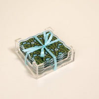 The Darling Effect's Everbloom Forest Green Table Talk Acrylic Coaster Set features dark floral coasters tied with a light blue ribbon in a clear holder—an elegant way to enhance your table décor.