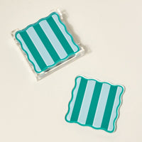 The Darling Effect’s Sicily Stripes Teal Table Talk Acrylic Coaster Set features two square coasters with wavy edges and teal stripes—one in a clear holder, one beside it—stylish, heat-resistant table décor for any space.
