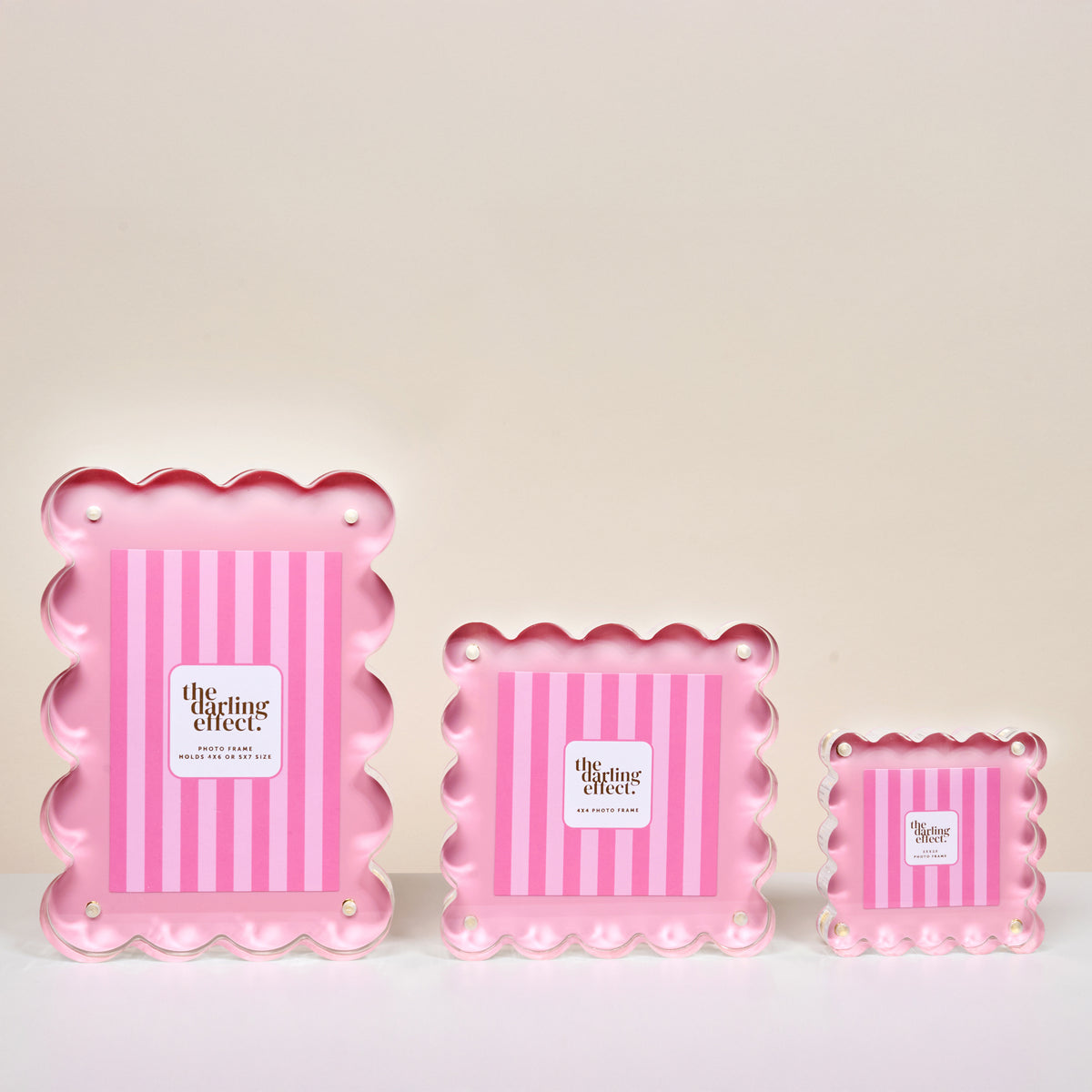 Three pink, scalloped-edge trays with vertical stripes and central labels reading "The Darling Effect" are inspired by the Blush Rectangle Scalloped Acrylic Picture Frame by The Darling Effect. The trays come in small, medium, and large sizes.