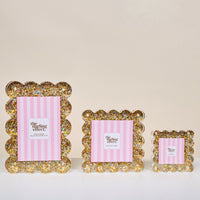 Three Gold Glitter Rectangle Scalloped Acrylic Picture Frames by The Darling Effect in graduated sizes are displayed with pink striped insert cards on a white surface against a neutral background.