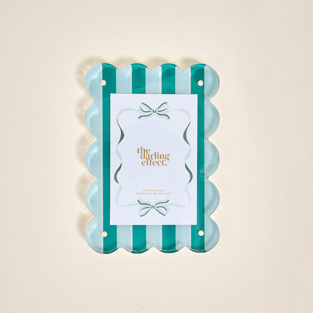 The Sicily Stripes Teal Rectangle Scalloped Acrylic Picture Frame by The Darling Effect features alternating teal and clear vertical stripes, holding a gold-lettered card, displayed on a light beige background.