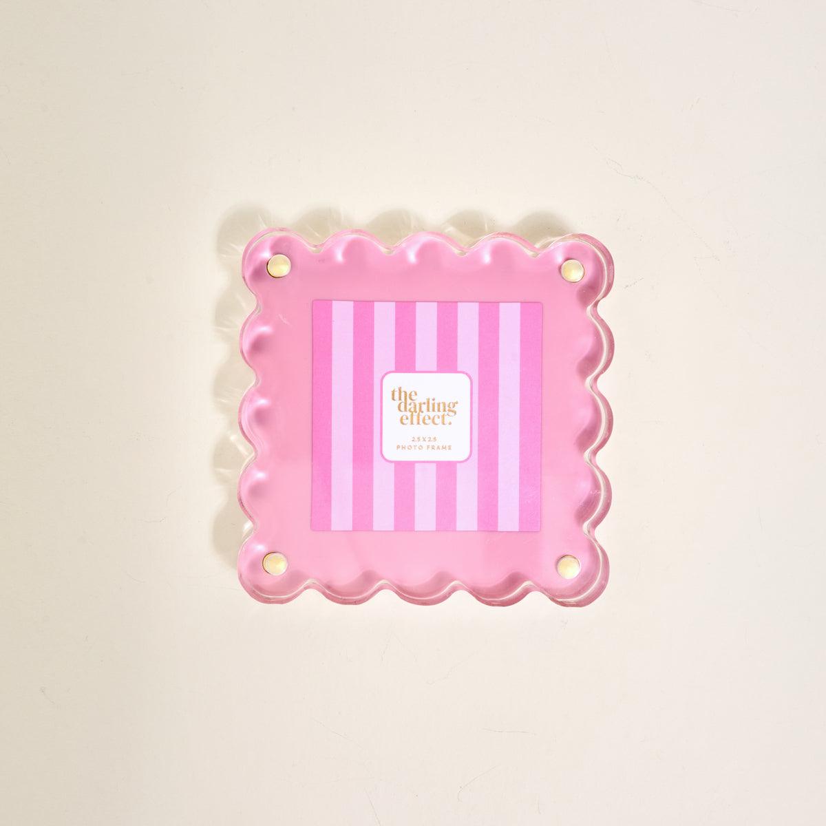 The Darling Effect's Blush Little Moments Acrylic Picture Frame is a pink, square frame with scalloped edges, vertical light and dark pink stripes, and four gold corner accents, shown against a plain light background.