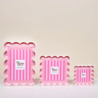 The Blush Little Moments Acrylic Picture Frame by The Darling Effect is shown against a light background, arranged from largest to smallest left to right. It features pink scalloped edges, vertical stripes, and the brand logo in the center.