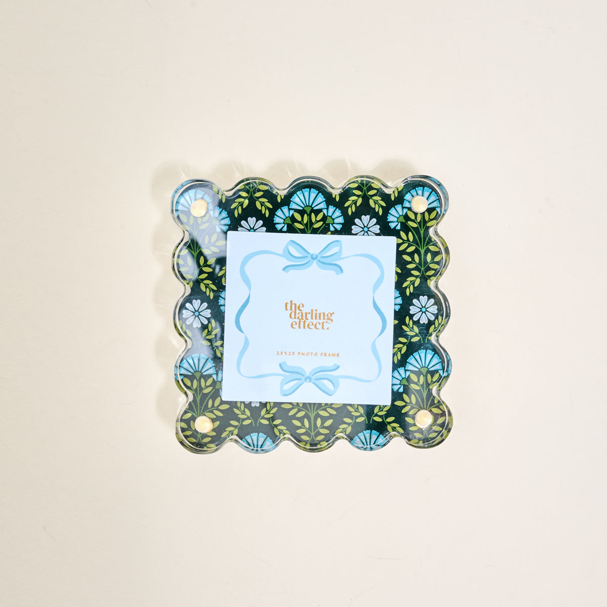 The Everbloom Forest Green Little Moments Acrylic Picture Frame by The Darling Effect features a scalloped edge with a dark green floral design, holding a light blue card and ribbon border. Fits 2.5x2.5 photos.