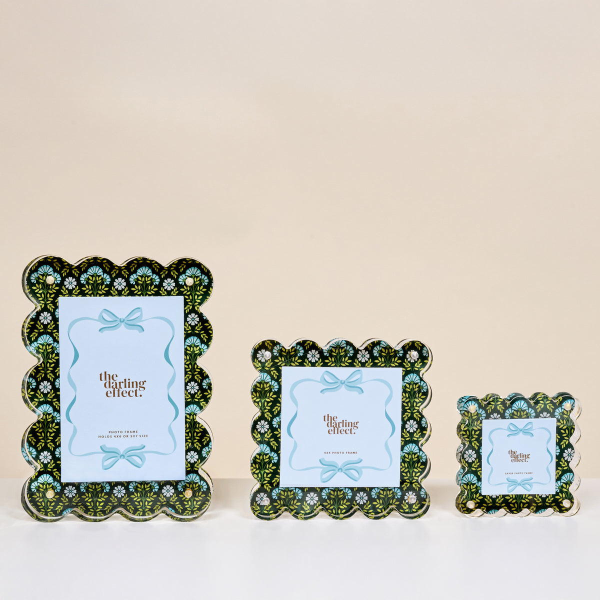 The Darling Effect’s Everbloom Forest Green Little Moments Acrylic Picture Frames, featuring scalloped edges and green, blue, and black floral designs, are shown in small, medium, and large sizes with placeholder cards against a neutral background.