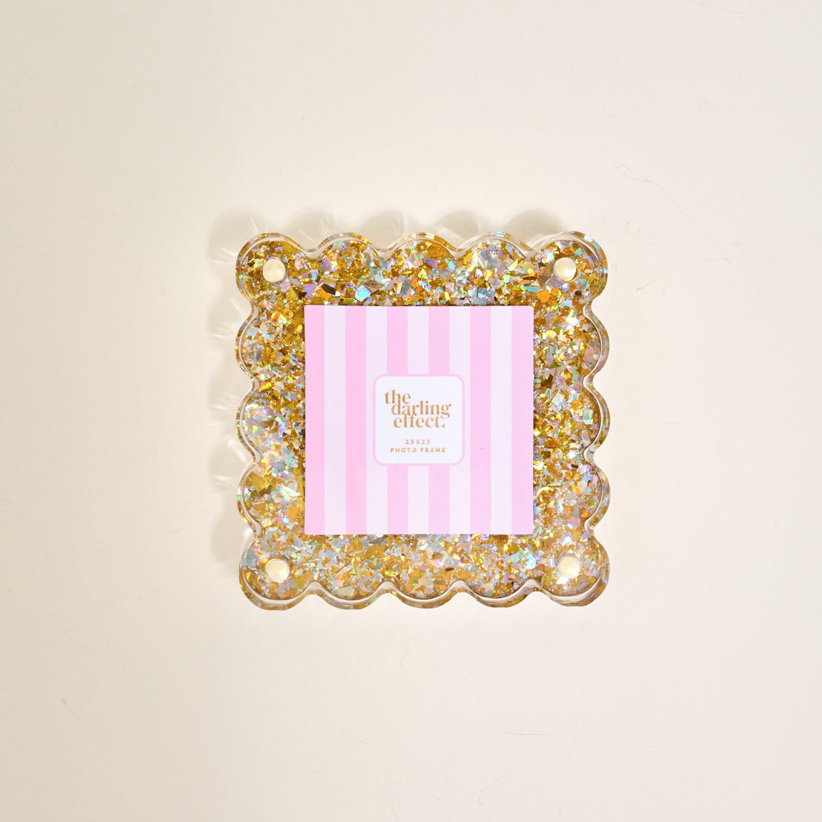The Gold Glitter Little Moments Acrylic Picture Frame by The Darling Effect features a square, scalloped-edge design with gold and silver glitter accents, shown with a pink and white striped card on a light background.