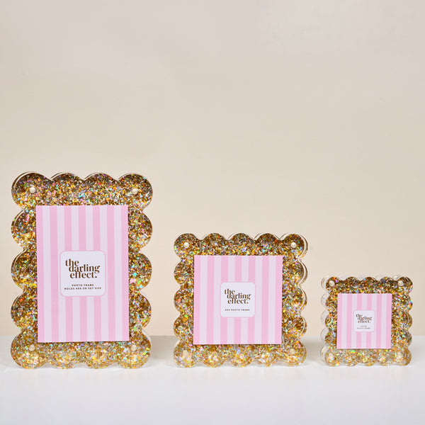 The Darling Effect Gold Glitter Little Moments Acrylic Picture Frame features scalloped edges, pink and white striped inserts, and a secure magnetic closure for easy display and access.