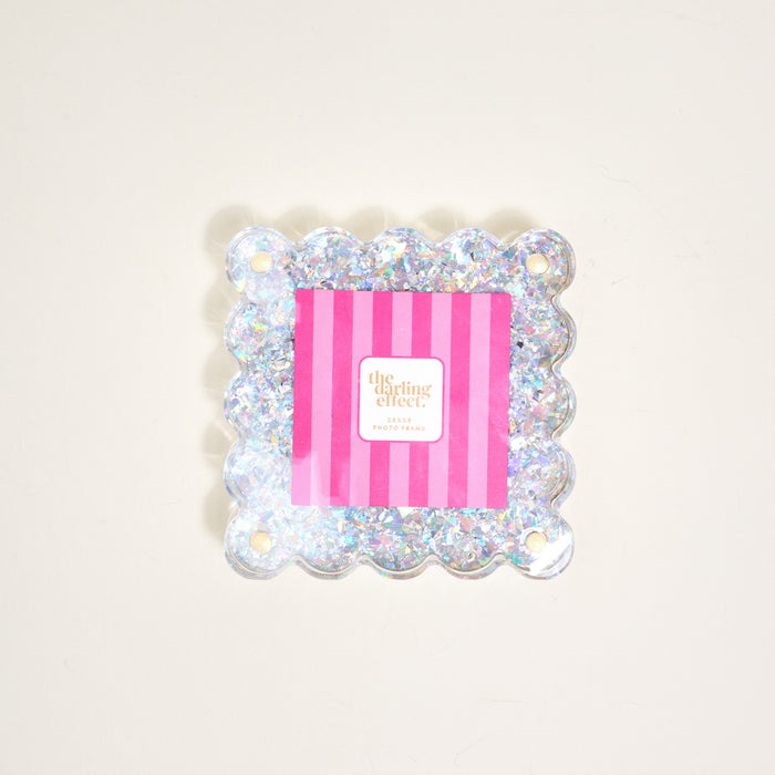 The Silver Glitter Little Moments Acrylic Picture Frame by The Darling Effect features a square, scalloped edge with glitter, a 2.5x2.5 photo space, pink and white striped insert, "the darling effect" text, and a magnetic closure.