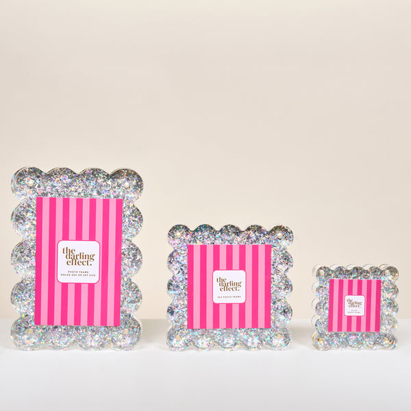 Three Silver Glitter Little Moments Acrylic Picture Frames by The Darling Effect are displayed. Each clear acrylic frame features iridescent sparkle and scalloped edges, with pink striped inserts in assorted sizes.