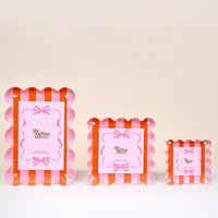 The Sicily Stripes Pink Little Moments Acrylic Picture Frames by The Darling Effect feature scalloped edges, magnetic closures, and pink papers with a bow design, available in small, medium, and large sizes against a pale background.